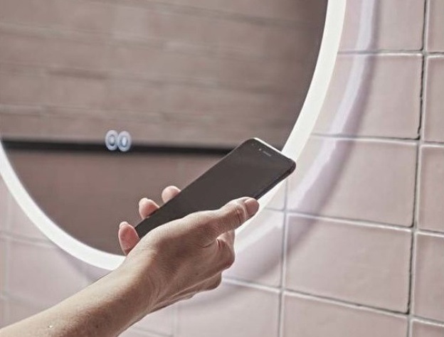 Product Lifestyle image of a man using his smart phone to control his Tavistock Resonate 600mm Circular Bluetooth Mirror